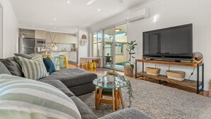 Un salon moderne avec un canapé d’angle, une table basse en verre et un téléviseur à écran plat posé sur un meuble en bois.