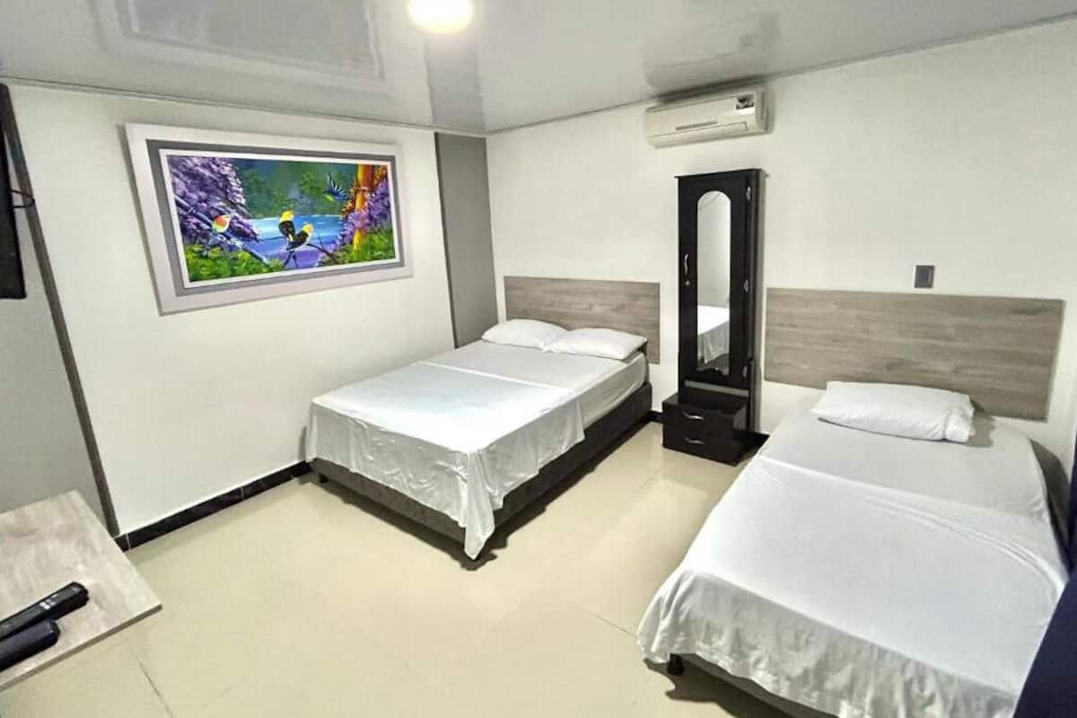 Une chambre d’hôtel avec deux lits simples, un grand miroir, un appareil de climatisation et un tableau au mur.