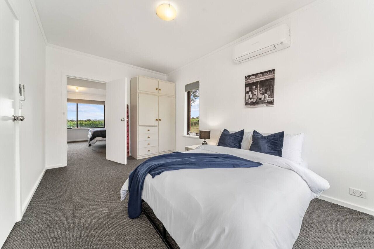 A bedroom with a bed, a wardrobe, a window, and a door leading to another room.
