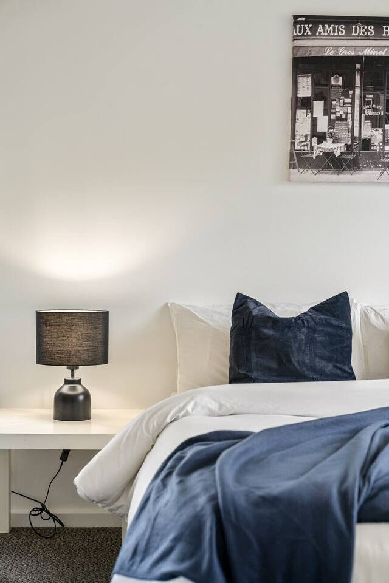 Un dormitorio con una cama, una mesita de noche con una lámpara y un cartel en la pared.