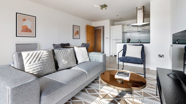 A modern living room with a grey sofa, a coffee table, and a blue chair. There is a kitchen in the background with white cabinets and a stove. - Blueground | Chalk Farm, terrace, nr Primrose Hill (London)