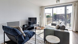 A modern living room with a sofa, armchair, and a coffee table. There is a television on a stand and a sliding glass door leading to a balcony. - Blueground | Chalk Farm, terrace, nr Primrose Hill (London)