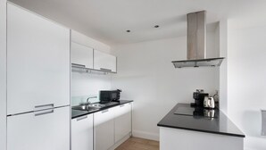 A modern kitchen with white cabinets, a black countertop, a microwave, and a kettle. - Blueground | Chalk Farm, terrace, nr Primrose Hill (London)