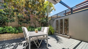 Une terrasse avec une table et des chaises, entourée de verdure et bordée d’un mur de briques.