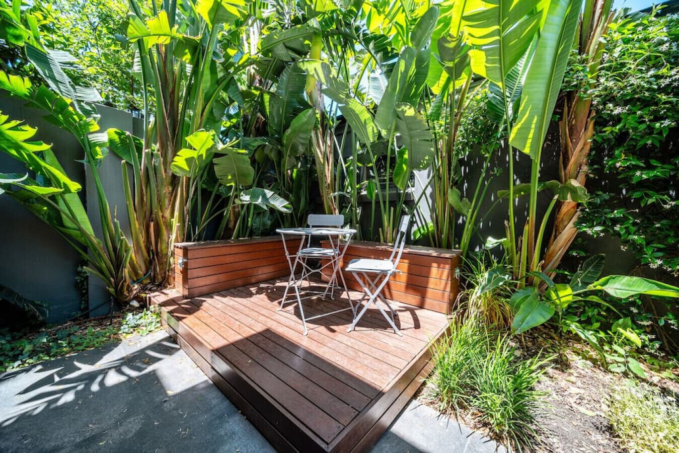 A wooden deck with a table and chairs surrounded by lush tropical plants.