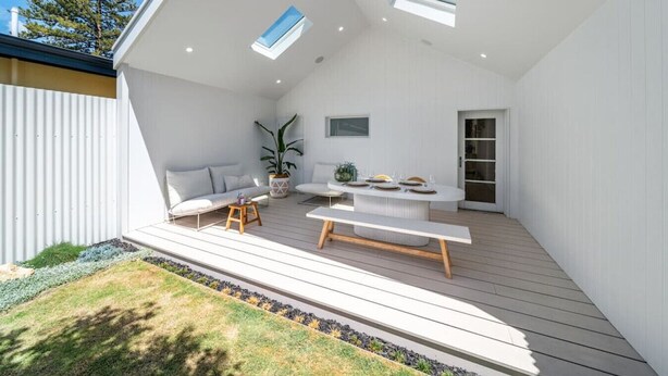 Une terrasse extérieure moderne, aménagée avec une table à manger, des sièges et un pot de fleurs.