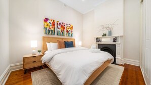 Une chambre moderne avec un grand lit, deux tables de chevet avec des lampes, une cheminée et des œuvres d’art colorées accrochées au mur.