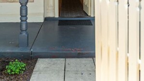Une entrée de maison avec un porche couvert, une clôture en bois et un chemin menant à la porte.