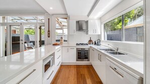 Une cuisine moderne avec des meubles blancs, un four encastré et une grande fenêtre qui laisse entrer la lumière naturelle.