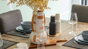 Una mesa de comedor con platos, tazones, vasos y un florero con flores secas.