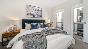A modern bedroom with a large bed, two bedside tables, a headboard, and a window with a view. - Urban Luxe—A Contemporary City-Edge Haven (Mile End)