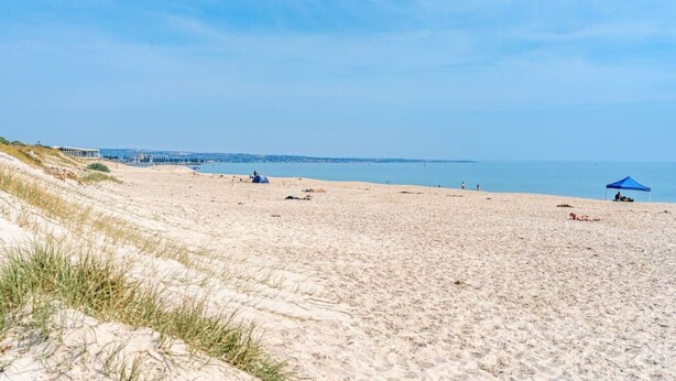 A beach with dunes, a clear sky, and a distant shoreline. - Sage By The Sea—Stylish Beachside Living with BBQ (West Beach)
