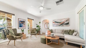 A modern living room with a sofa, two armchairs, a coffee table, and a ceiling fan. - Sage By The Sea—Stylish Beachside Living with BBQ (West Beach)