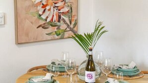 A round dining table set with teal plates, wine glasses, and a bottle of wine. - Sage By The Sea—Stylish Beachside Living with BBQ (West Beach)