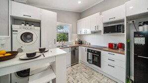 A modern kitchen with white cabinets, a built-in washing machine, a microwave, a refrigerator, and a wooden countertop.