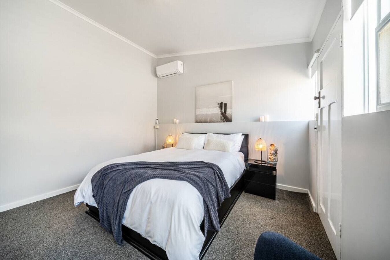 A modern bedroom with a bed, bedside tables, a wall-mounted air conditioner, and a window.