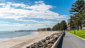 A coastal road with a beach on one side and a row of buildings on the other.