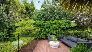 Eine Terrasse mit Holzdeck, einem runden weißen Tisch und einer schwarzen Couch.
