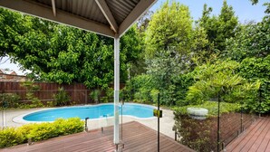 Eine Holzterrasse mit Swimmingpool, umgeben von üppigem Grün und einem Holzzaun.