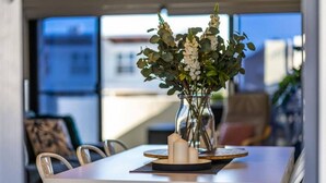 A dining table with a vase of flowers, candles, and a glass of water. - Higher Ground on Seaview - Rooftop Coastal Escape (West Beach)