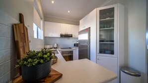 A modern kitchen with white cabinets, a stainless steel refrigerator, and a wooden countertop with a potted plant. - Higher Ground on Seaview - Rooftop Coastal Escape (West Beach)