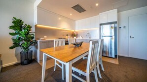 Une cuisine moderne avec des meubles blancs, une table à manger en bois et un réfrigérateur en acier inoxydable.