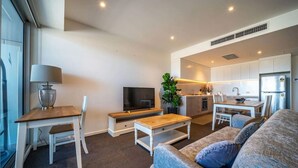 Un salon moderne avec un téléviseur, un canapé et une table basse. Il y a également un coin cuisine équipé de placards et d’un réfrigérateur.