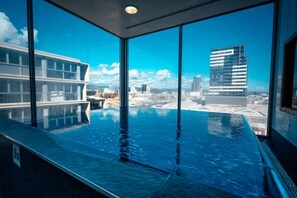 A modern indoor swimming pool with a city view, large windows, and a clean, contemporary design. - Infinity on Morphett—Stay Central in the CBD (Adelaide)