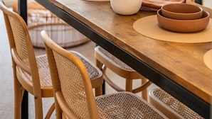 Un coin repas avec une table en bois, des chaises marron et un vase blanc contenant des feuilles séchées.