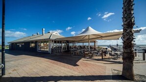 An outdoor seating area with tables and umbrellas, a building labeled 'Orange Jet Cafe', and a palm tree. - Urban Beach Shack - Steps to Grange Beach & Café (Grange)
