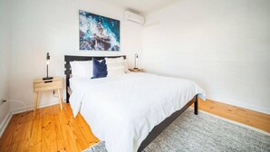 A bedroom with a bed, a nightstand, a lamp, a painting, and a white wall. - Urban Beach Shack - Steps to Grange Beach & Café (Grange)