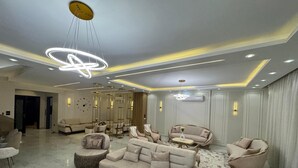 A modern living room with a large beige sofa, a coffee table, and a TV. There are several chairs and a decorative floor lamp. - villa with garden in continental COMP (Sheikh Zayed City)