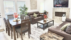 A modern living room with a brown leather sofa, a dining table with chairs, a coffee table, and a fireplace. - Arlington Entertainment District Home Orange Door (Arlington)