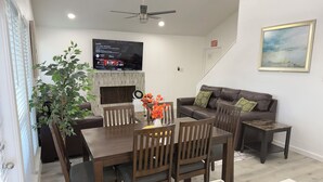 A modern living room with a dining area, a fireplace, a flat-screen TV mounted on the wall, and a ceiling fan. - Arlington Entertainment District Home Orange Door (Arlington)