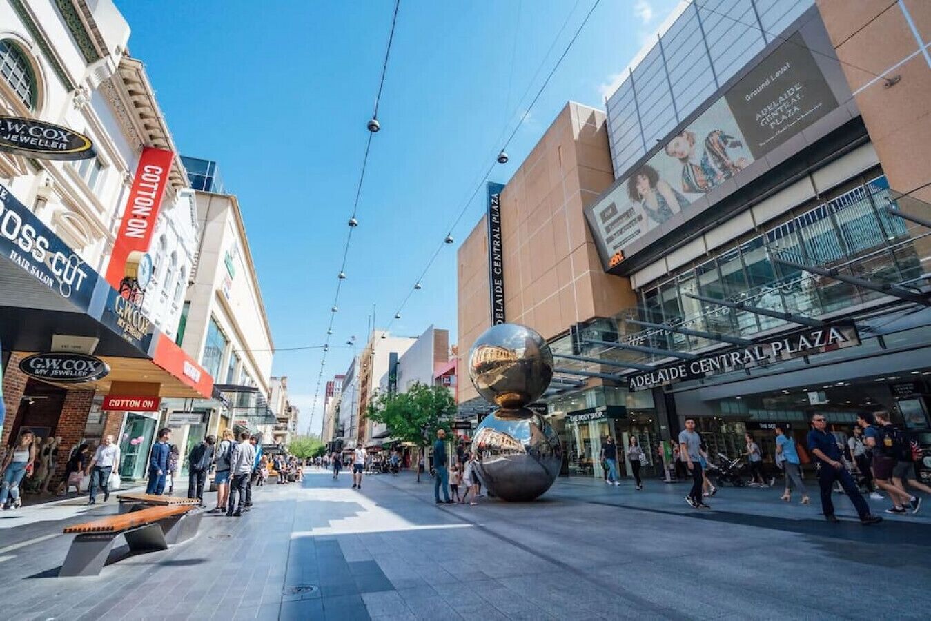 A busy urban street with shops and a large spherical sculpture in the center.