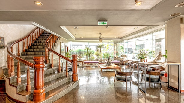 A spacious lobby with a curved wooden staircase, a seating area with tables and chairs, and large windows offering a view of the outdoors. - FORTUNE HOTEL (Xinyi)