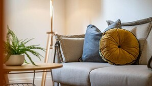 A living room with a sofa, a floor lamp, a small table with a plant, and a framed picture on the wall. - Irma`s Place—A Historic Garden Cottage (Adelaide)