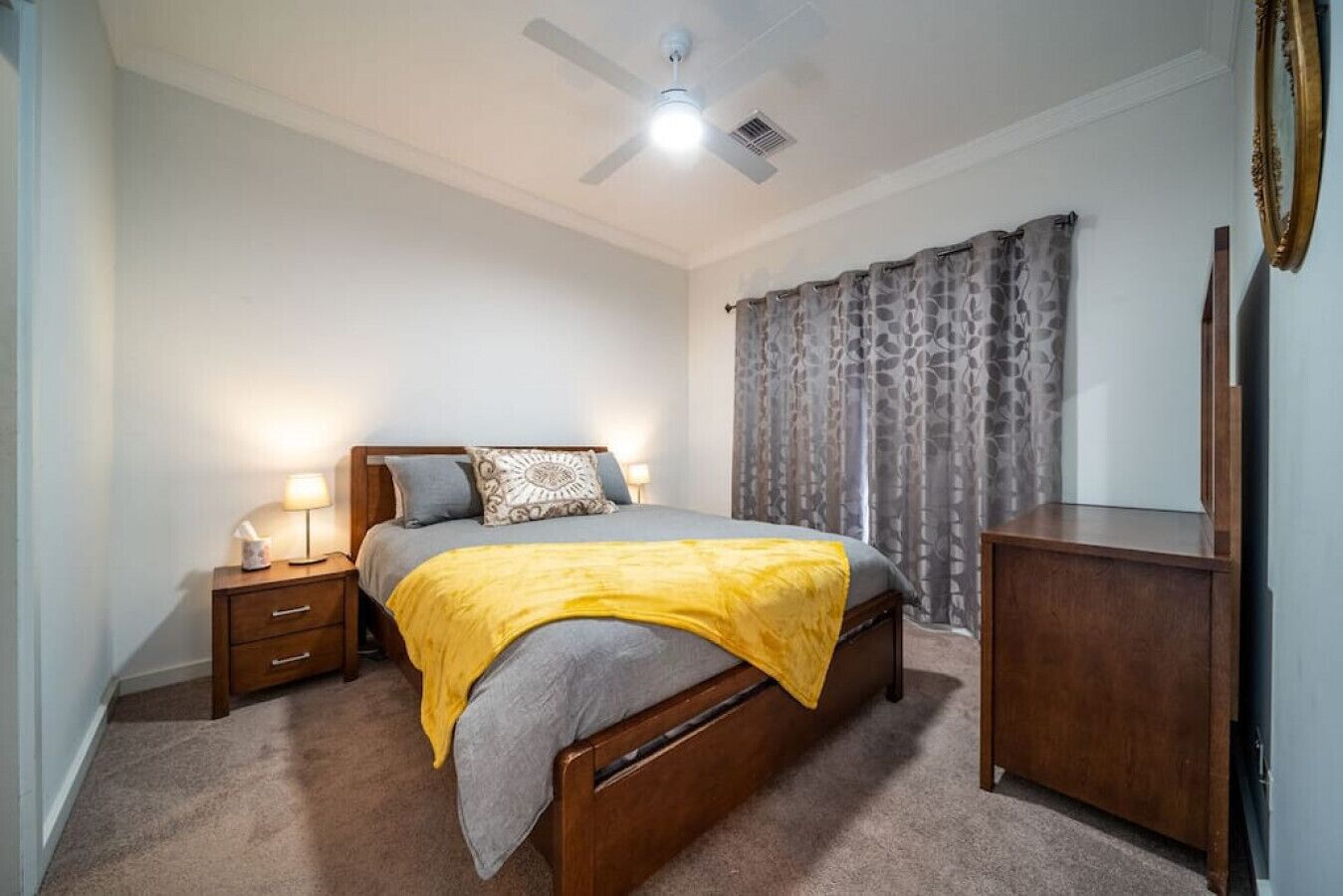 A bedroom with a bed, bedside tables, a dresser, a ceiling fan, and curtains.