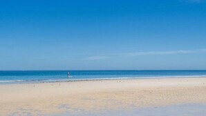 Une plage avec un ciel dégagé, une personne debout dans l’eau et une rive sablonneuse.