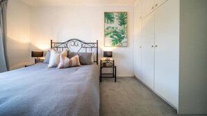 Een slaapkamer met een bed, nachtkastjes, een kledingkast en een plant in een lijst aan de muur.