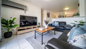 Een moderne woonkamer met een flatscreen televisie, een salontafel, een bank en een potplant.