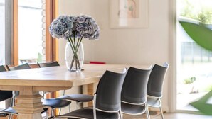 A dining area with a wooden table and black chairs, a vase with flowers, and a framed picture on the wall. - Summer Breeze—A Coastal Poolside Retreat (Glenelg East)