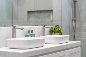 Ein modernes Badezimmer mit zwei weißen Waschbecken, einer kleinen Topfpflanze und einer Duschkabine.