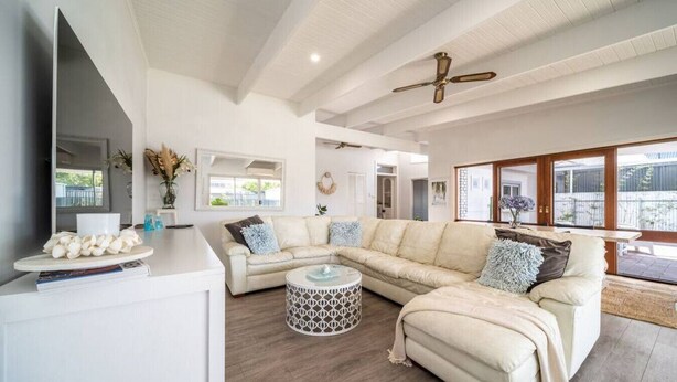 A spacious living room with a large beige sectional sofa, a round coffee table, and a white console table with decorative items. - Summer Breeze—A Coastal Poolside Retreat (Glenelg East)