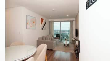 Ein modernes Wohnzimmer mit Glastür zum Balkon, einem Essbereich mit rundem Tisch und einem an der Wand befestigten Flachbildfernseher.