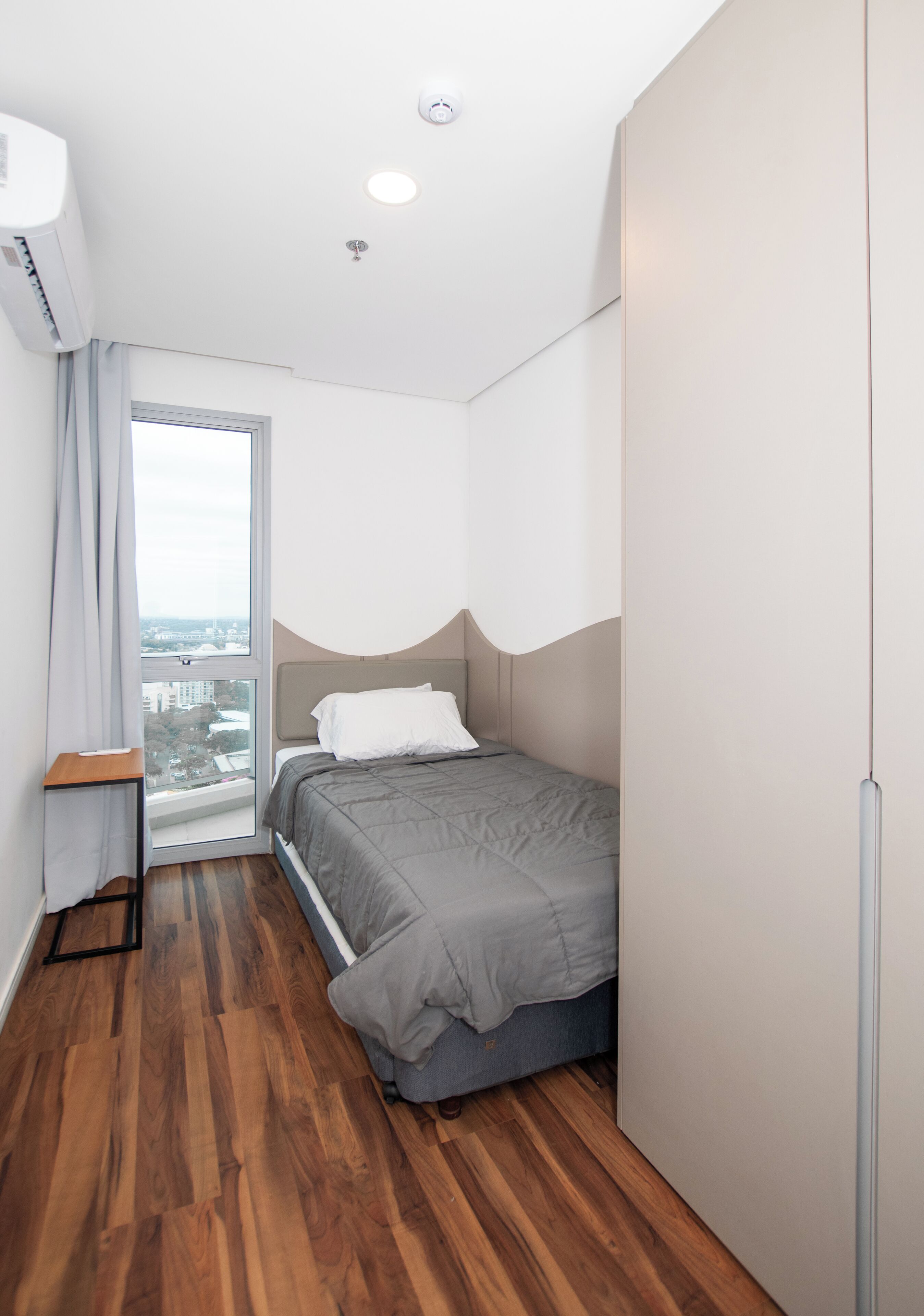 Un dormitorio pequeño con cama, una mesita y ventana con vistas.