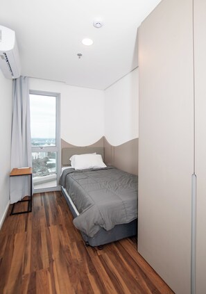 A compact bedroom with a bed, a small table, and a window with a view.