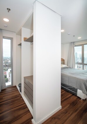 A bedroom with a bed, a wardrobe, a window with a city view, and a door.