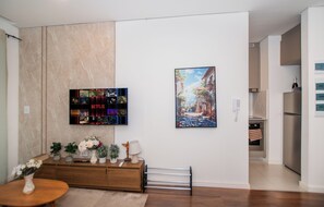 A modern living room with a flat-screen TV mounted on the wall, a wooden console table with decorative items, and a framed painting above it. - Luxurious 2-bedroom with gym, pool and AC in the best location of Asunción (Asunción)