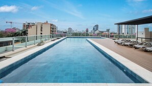 Ein Pool auf dem Dach mit Blick auf die Stadt, Liegestühlen und einer Holzterrasse.